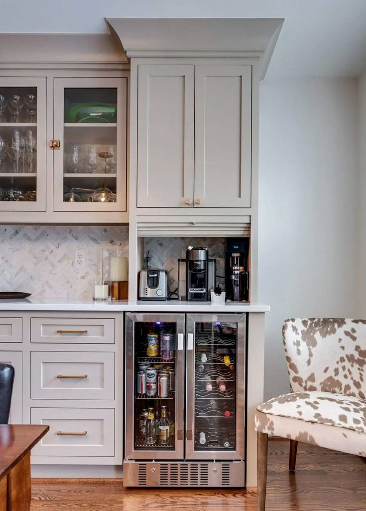 a kitchen with white cabinets and wooden flooring has an icebox in the corner