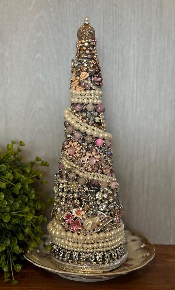 a christmas tree made out of buttons and pearls on a silver platter next to a potted plant