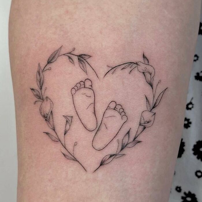 a heart shaped tattoo with a baby's foot in the center and leaves around it