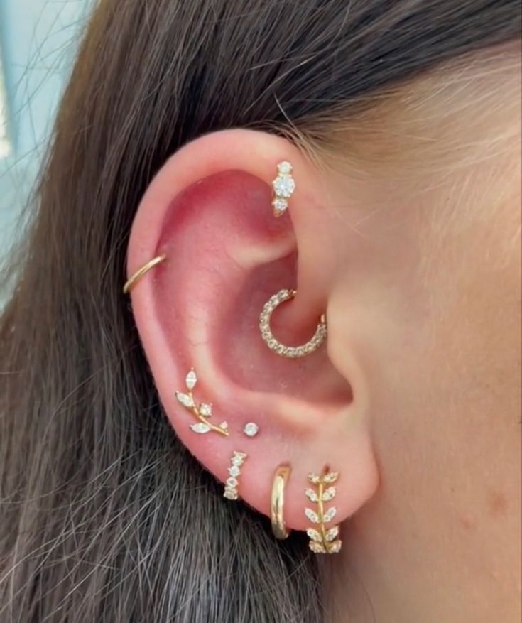 a woman with ear piercings on her left side is wearing an ear cuff and has three small leaves attached to it