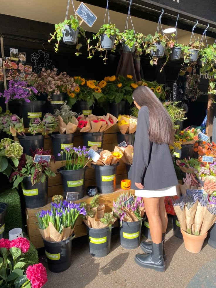 a woman standing in front of a bunch of flowers at a flower shop with lots of potted plants hanging from the ceiling