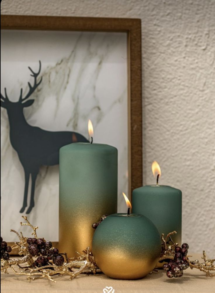 three teal candles sitting on top of a table next to a framed deer head