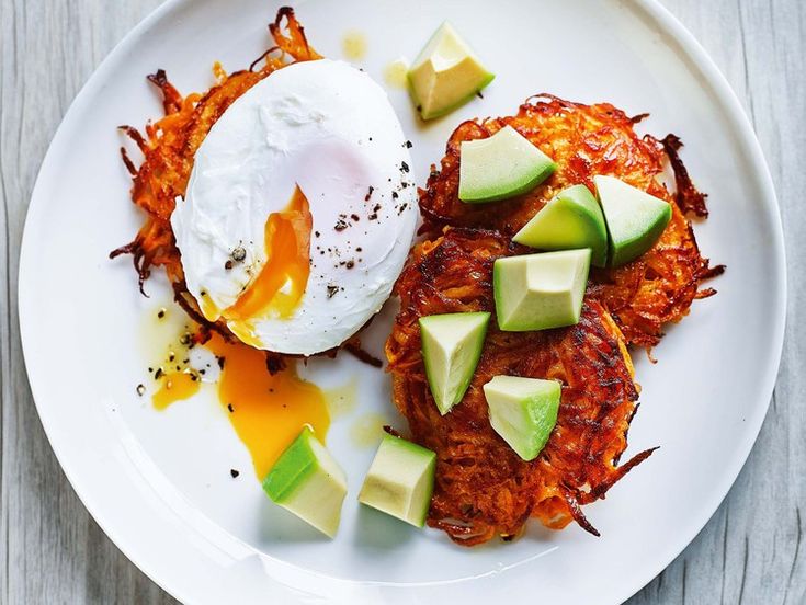 an egg is sitting on top of some hash browns with avocado and sliced cucumbers