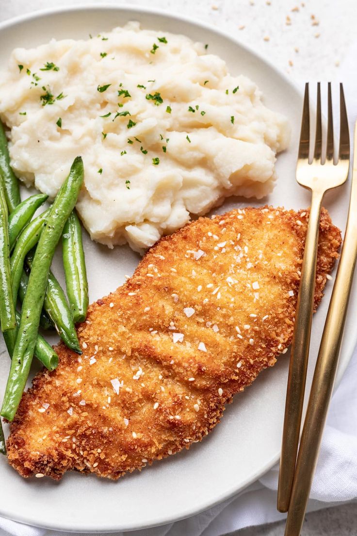 a white plate topped with fish, mashed potatoes and green beans next to a fork