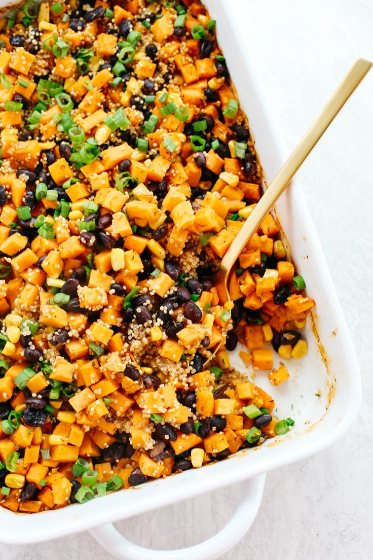 a casserole dish filled with black beans, green onions and cheese topped with a wooden spoon