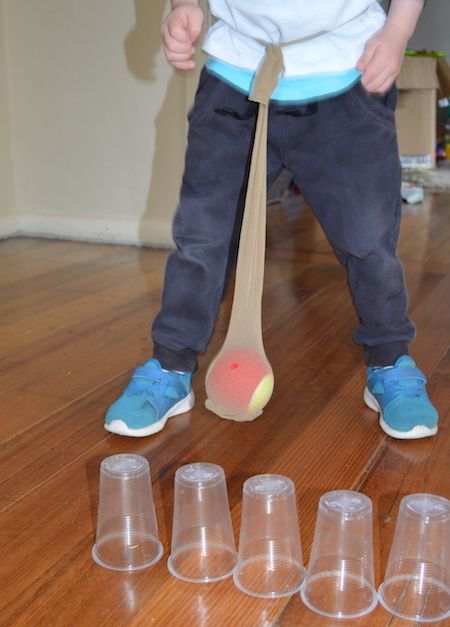 a young child standing on the floor with plastic cups and a wooden spoon