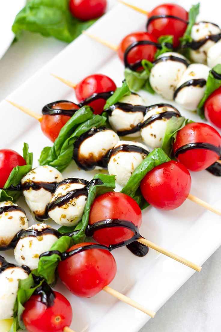 tomatoes and mozzarella skewers on a white plate with lettuce