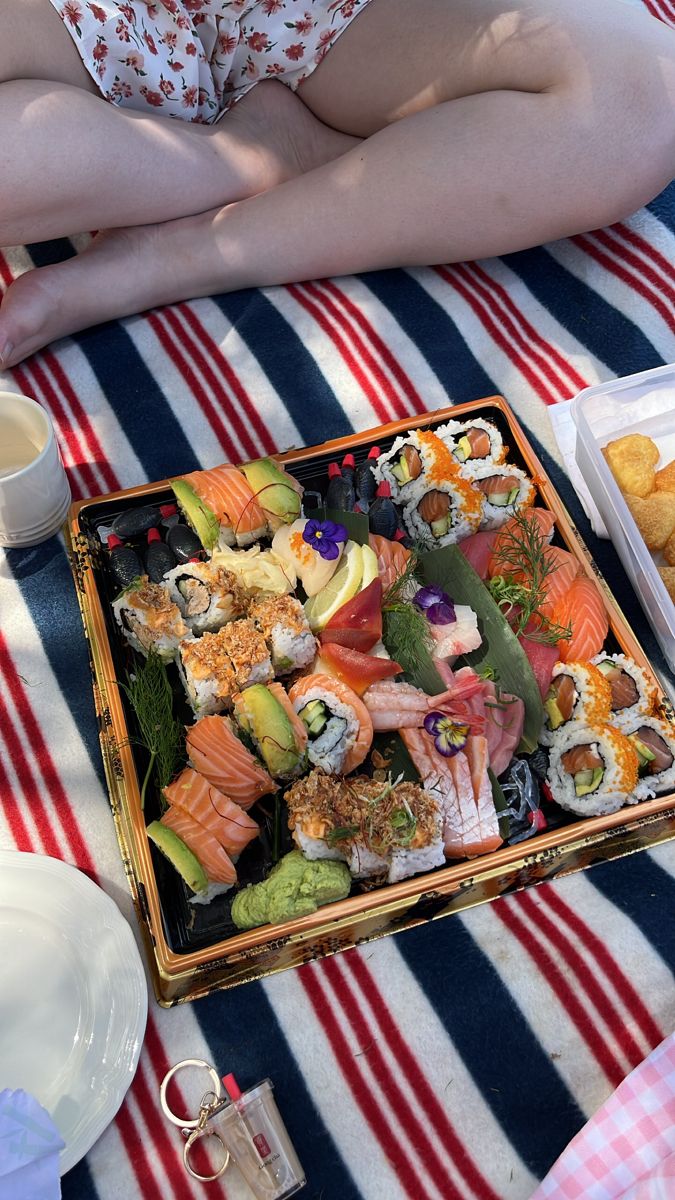 a woman sitting in front of a tray of sushi on a table with other food