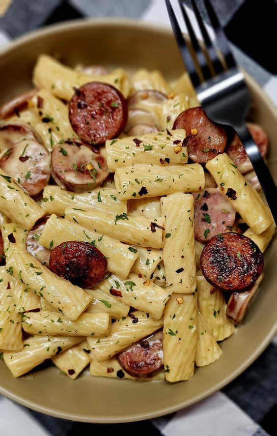 a bowl filled with pasta and sausages on top of a checkered table cloth