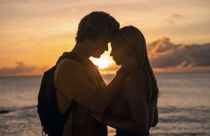 two people standing next to each other in front of the ocean at sunset or sunrise