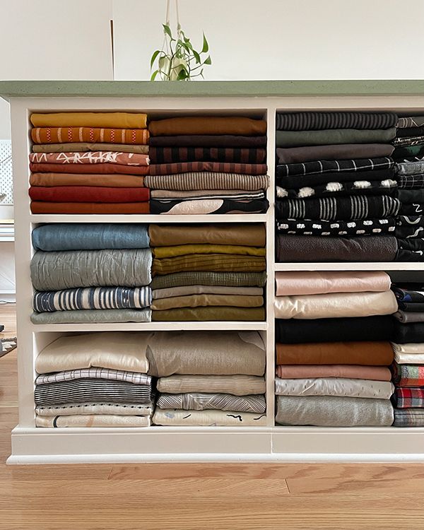 a white cabinet filled with folded clothes on top of a hard wood floor next to a potted plant