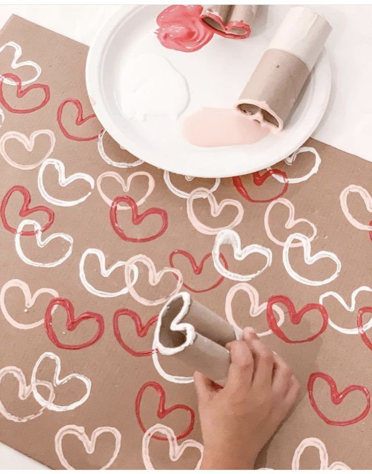 someone is painting hearts on a table with wax paper and some other crafting supplies