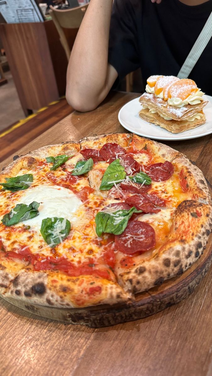 a pizza sitting on top of a wooden table next to a white plate with food