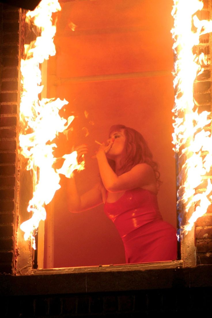 a woman standing in front of a mirror with fire coming out of it's sides