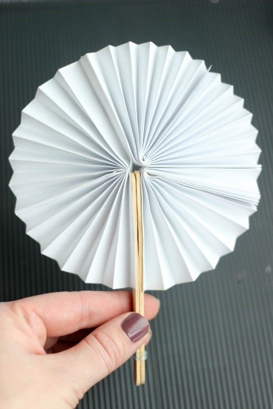 a hand holding a white paper fan with wooden sticks sticking out of it's center