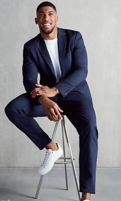 a man sitting on top of a stool wearing a blue suit and white sneakers with his hands in his pockets