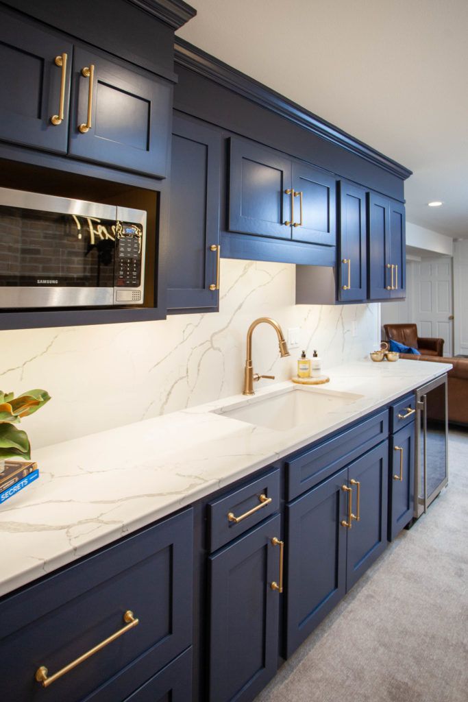 a kitchen with blue cabinets and white counter tops, gold handles on the faucet