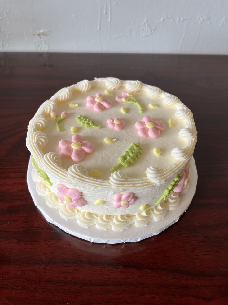 a cake with white frosting and pink flowers on it sitting on a wooden table