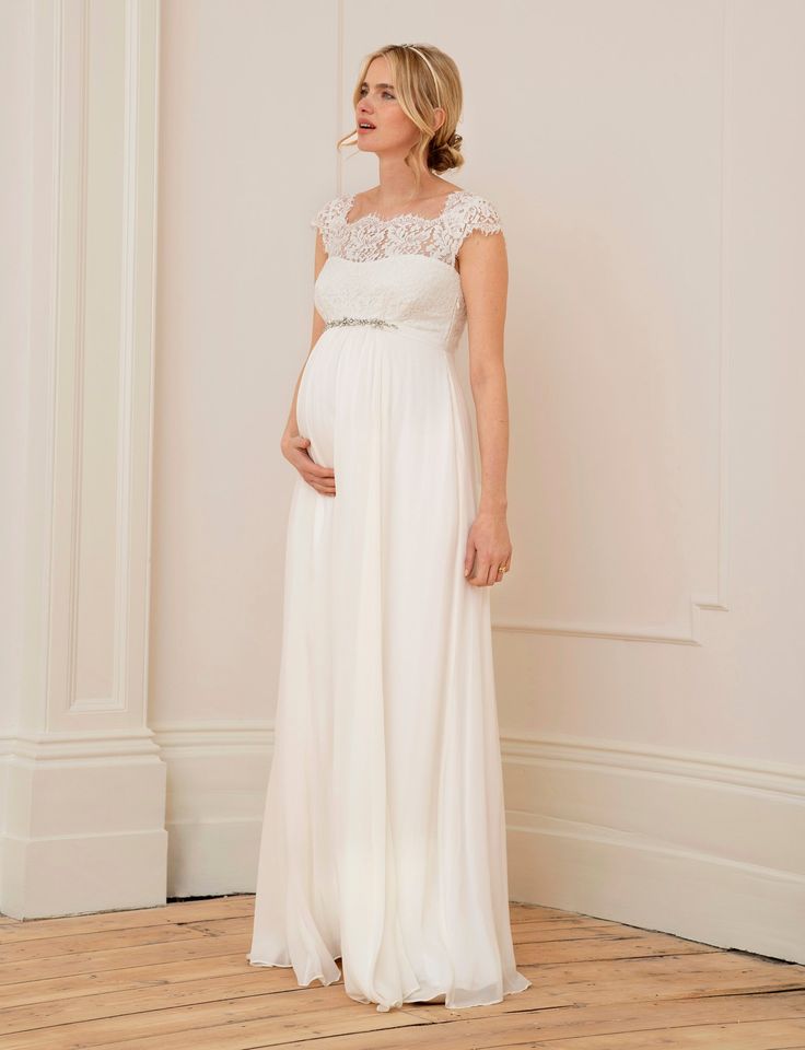 a pregnant woman in a white gown standing against a wall