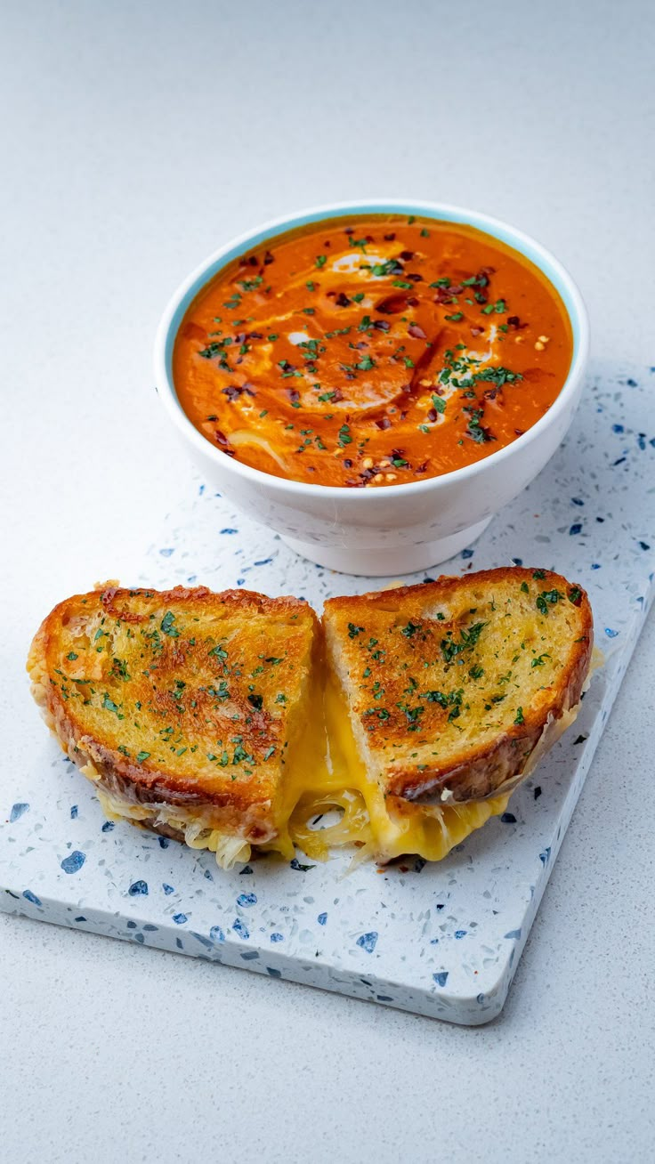 a grilled cheese sandwich cut in half with a bowl of soup on the side