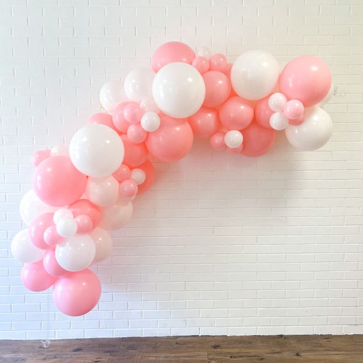 pink and white balloons are arranged in the shape of an arch on a brick wall