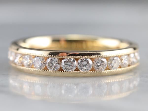 a yellow gold wedding ring with five diamonds on the inside and outside, sitting on a reflective surface