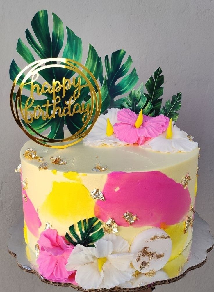 a birthday cake decorated with tropical leaves and flowers