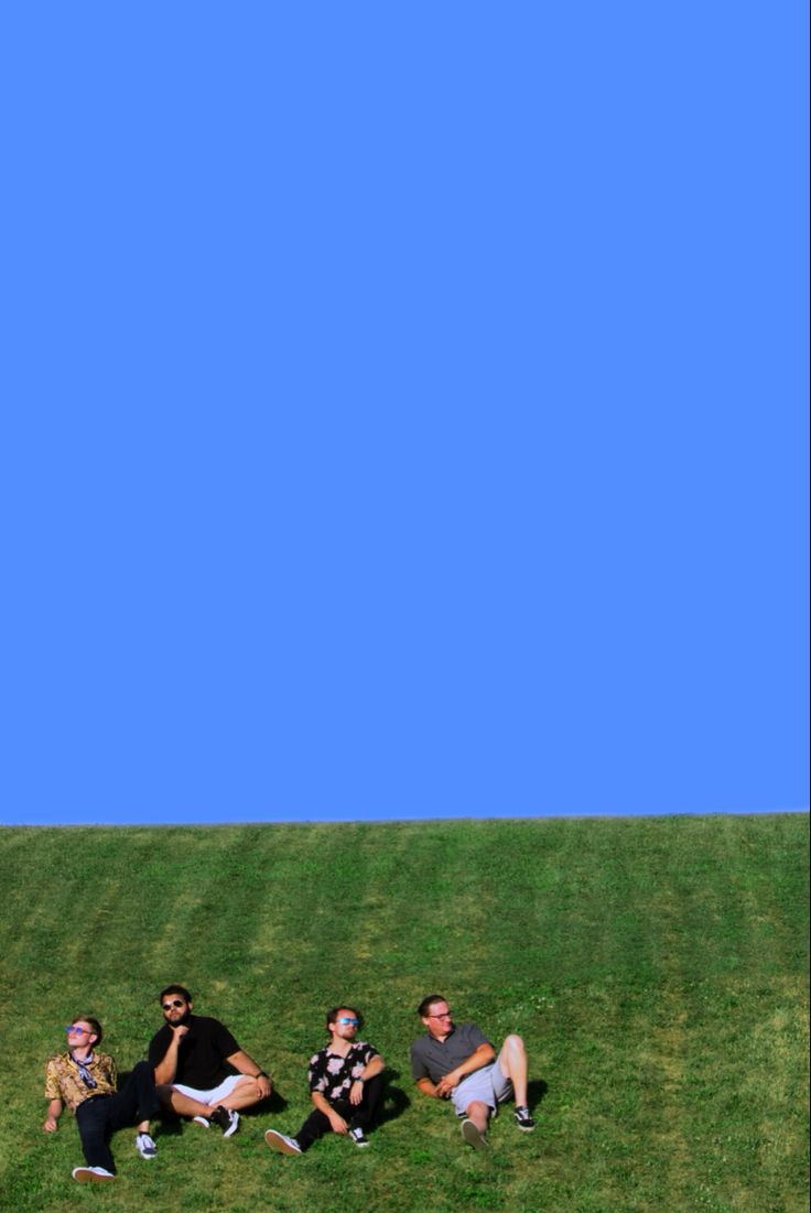 three people sitting in the grass with a cell phone