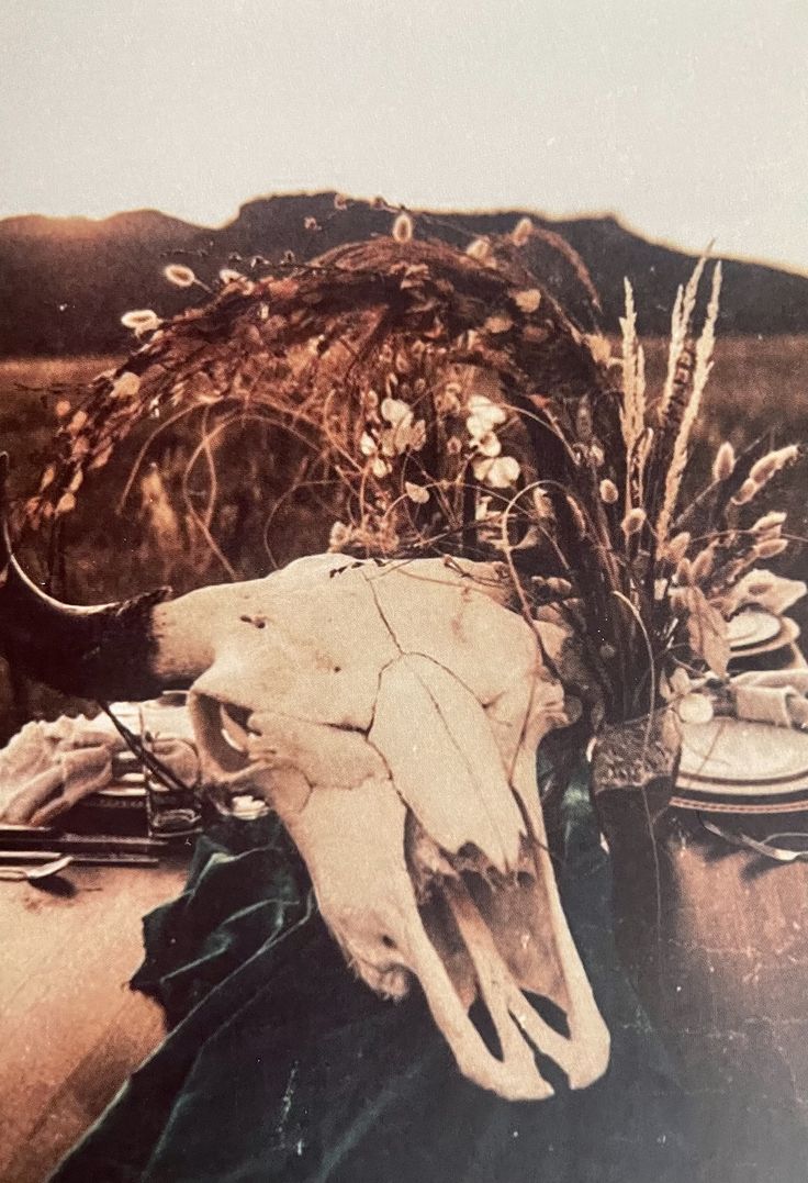 an animal's skull is sitting on a table with other items and flowers in the background