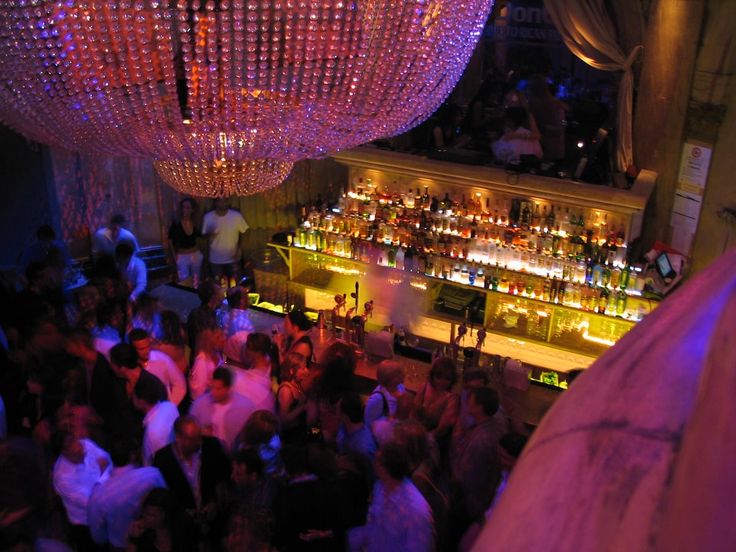 a crowded bar with lots of people at the bar and chandeliers hanging from the ceiling