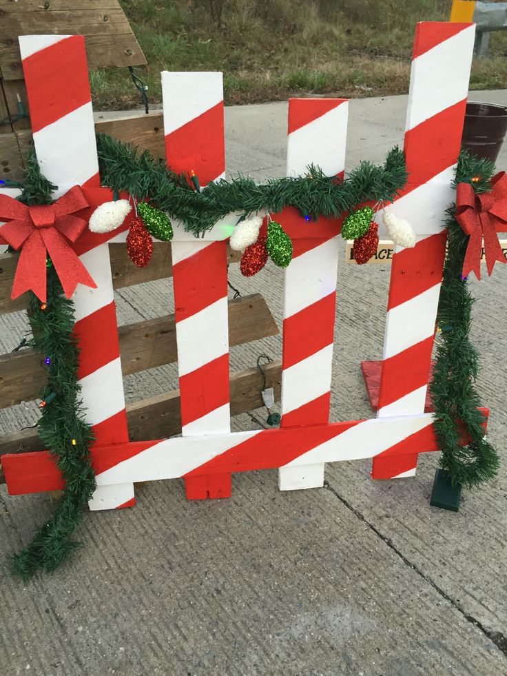 a wooden fence decorated with red and white striped christmas garlands, bows and poinsettis