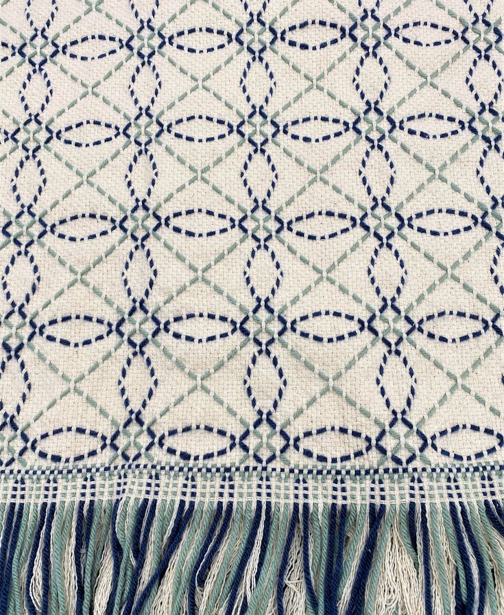 a blue and white throw with fringes on it's edges, in the shape of circles