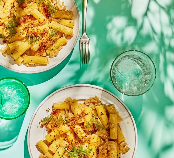 two white plates with food on them next to glasses and silverware, one plate has broccoli and the other is pasta