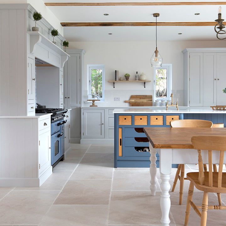 a kitchen with blue and white cabinets, an island table and two chairs in it