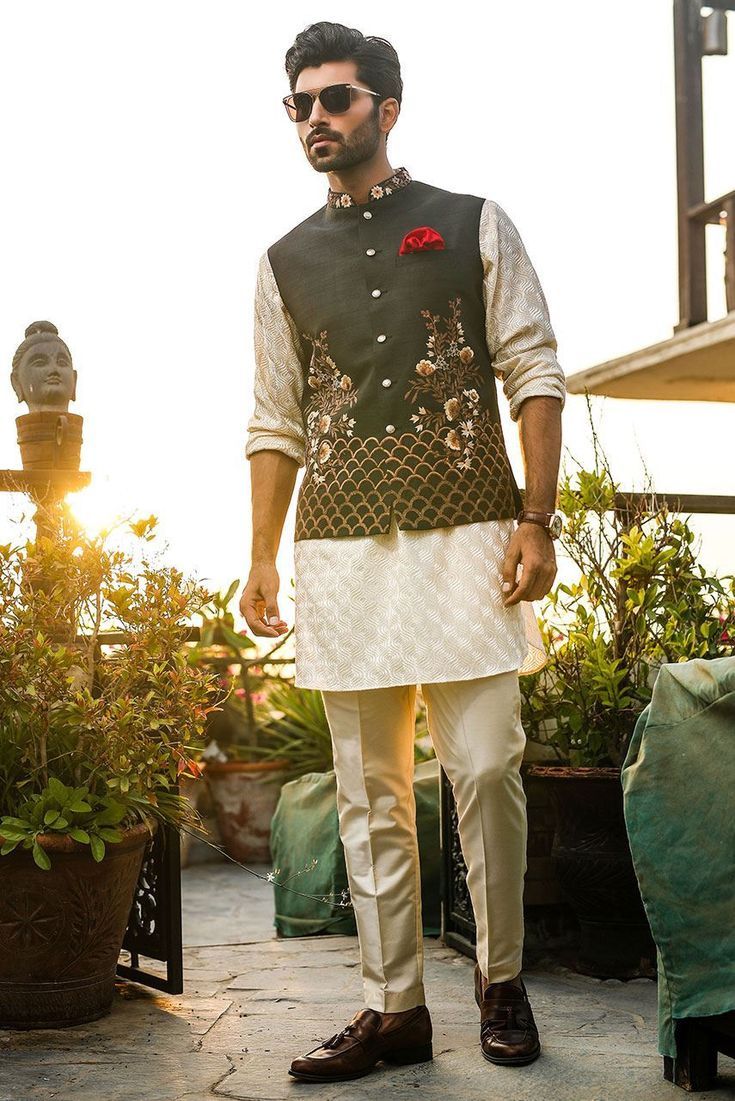 a man standing in front of some potted plants wearing a white and black outfit