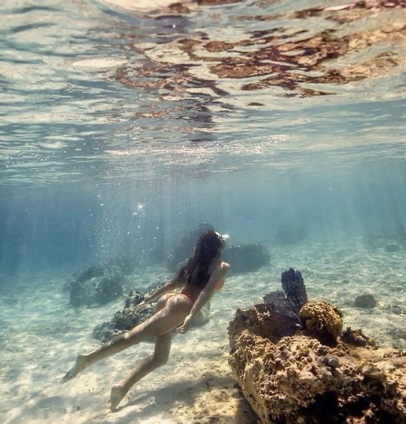 a woman is swimming in the ocean with rocks and corals on the water's surface