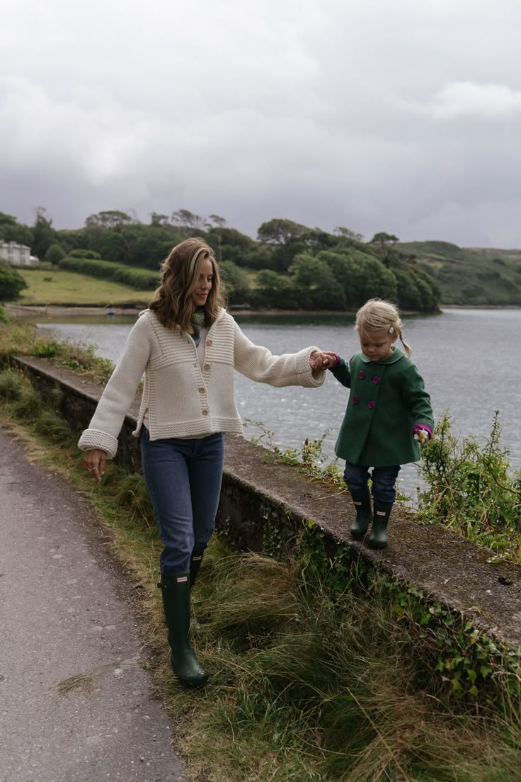 a woman holding the hand of a little boy on a path near a body of water