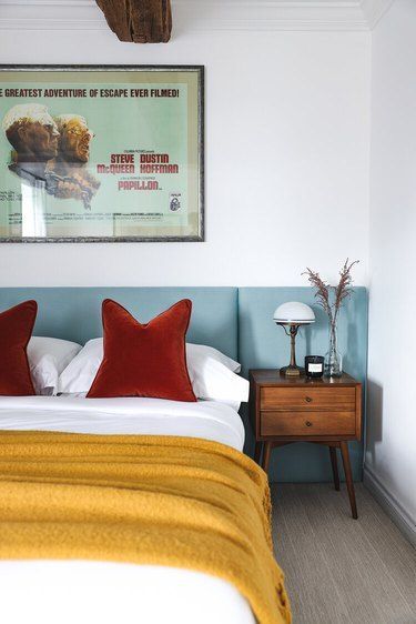 a bed with two red pillows on top of it next to a night stand and lamp