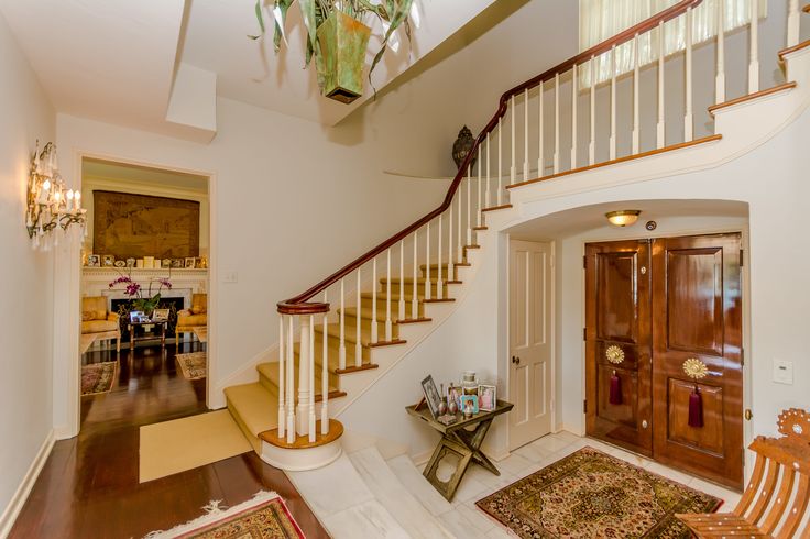 a staircase leading up to a living room and dining room area with rugs on the floor