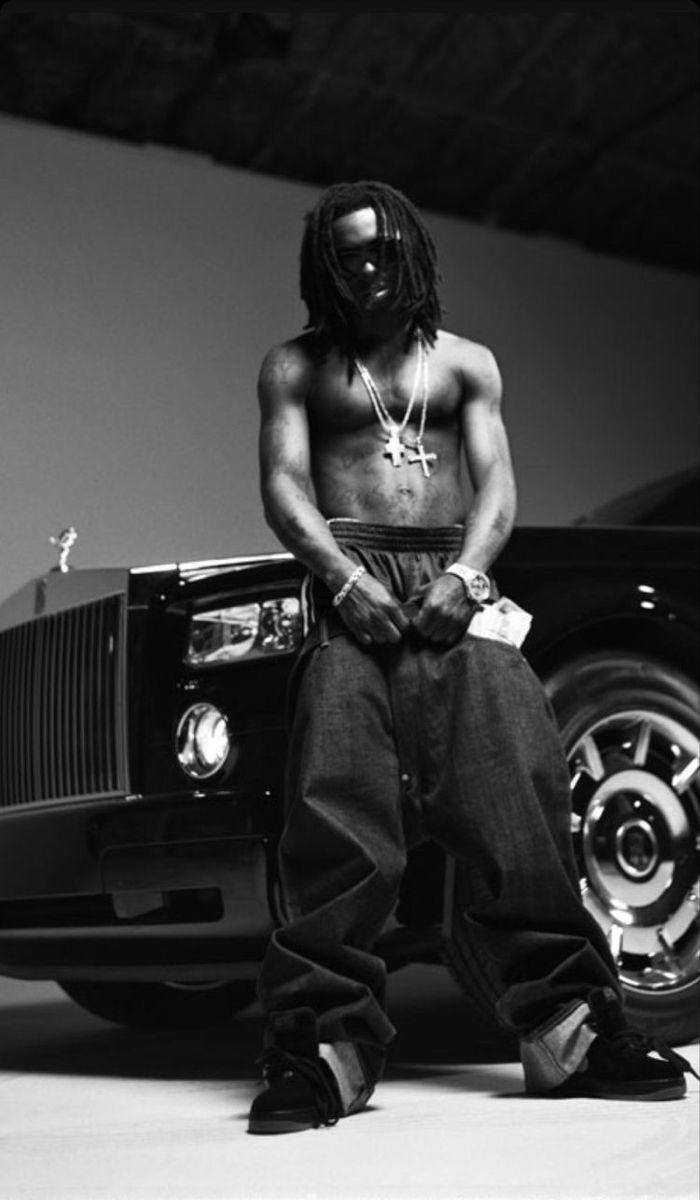 a man sitting on top of a car next to a black and white photo with his hands in his pockets