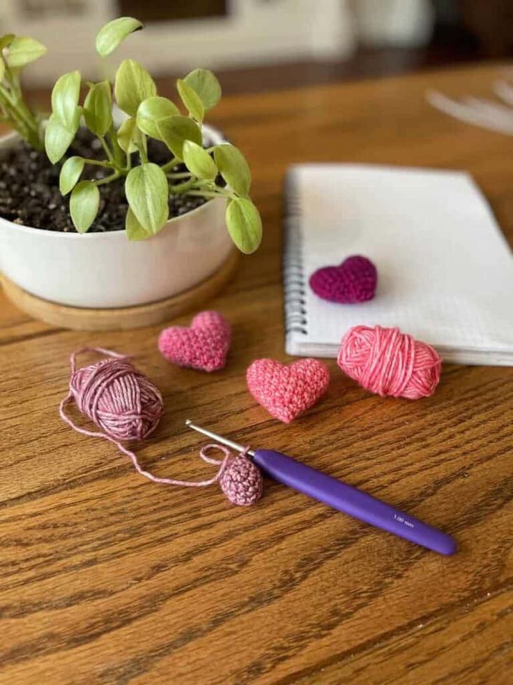 crochet hearts and yarn on a wooden table next to a potted plant