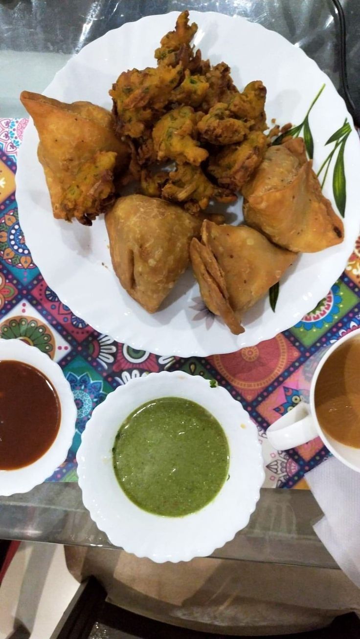 a plate with some food on it next to two cups of tea and sauces