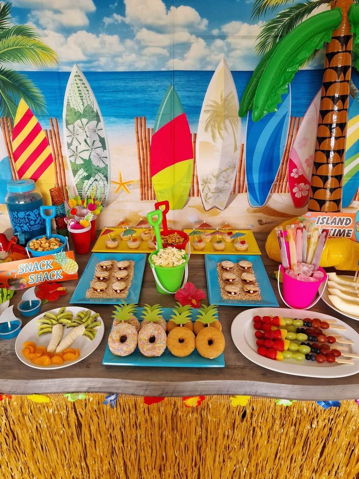 a table topped with lots of food next to a wall covered in surfboards and palm trees