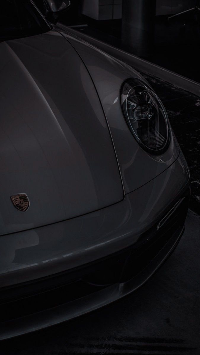 the front end of a black sports car in a dimly lit garage with its lights on