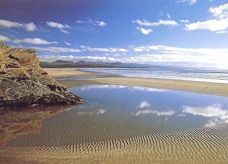 the sky is reflected in the still water on the beach near the rocks and sand