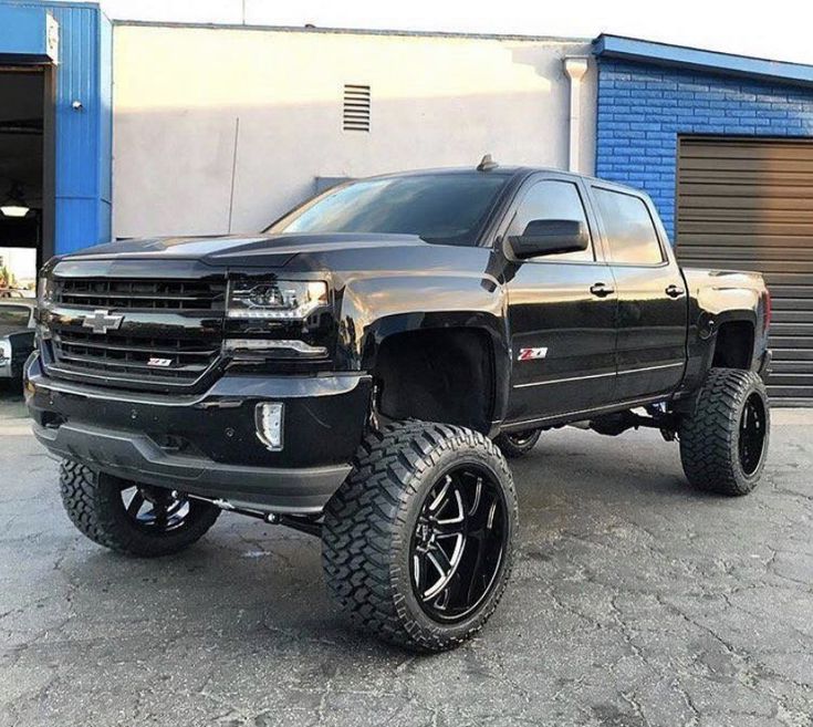 a large black truck parked in front of a blue building with two tires on it