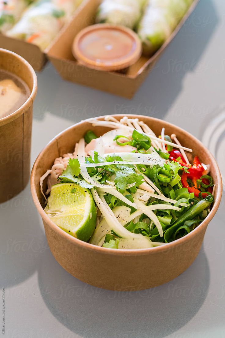 two brown bowls filled with food on top of a white table next to cups and sauces