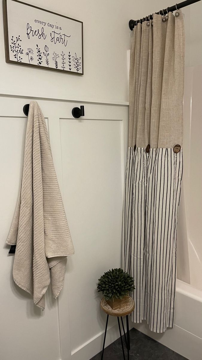 a white bathroom with black and white striped towels hanging on the shower curtain, next to a small potted plant