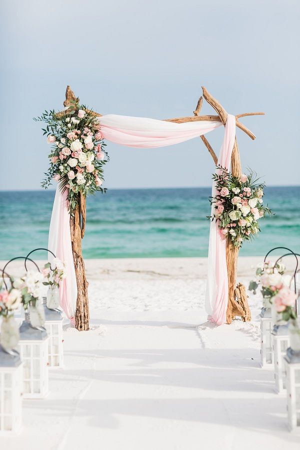 an outdoor wedding setup on the beach with pink and white flowers, greenery and candles