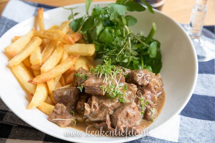 a white plate topped with meat and fries on top of a checkered table cloth